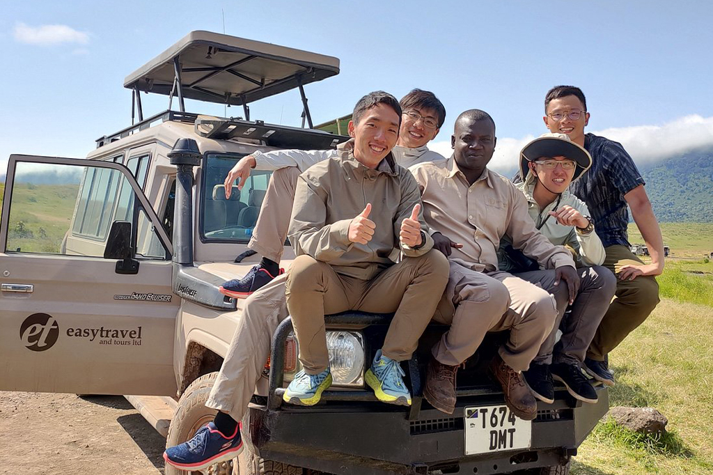 Group of tourists sitting with Ombeni Alfayo on top of the safari vehicle