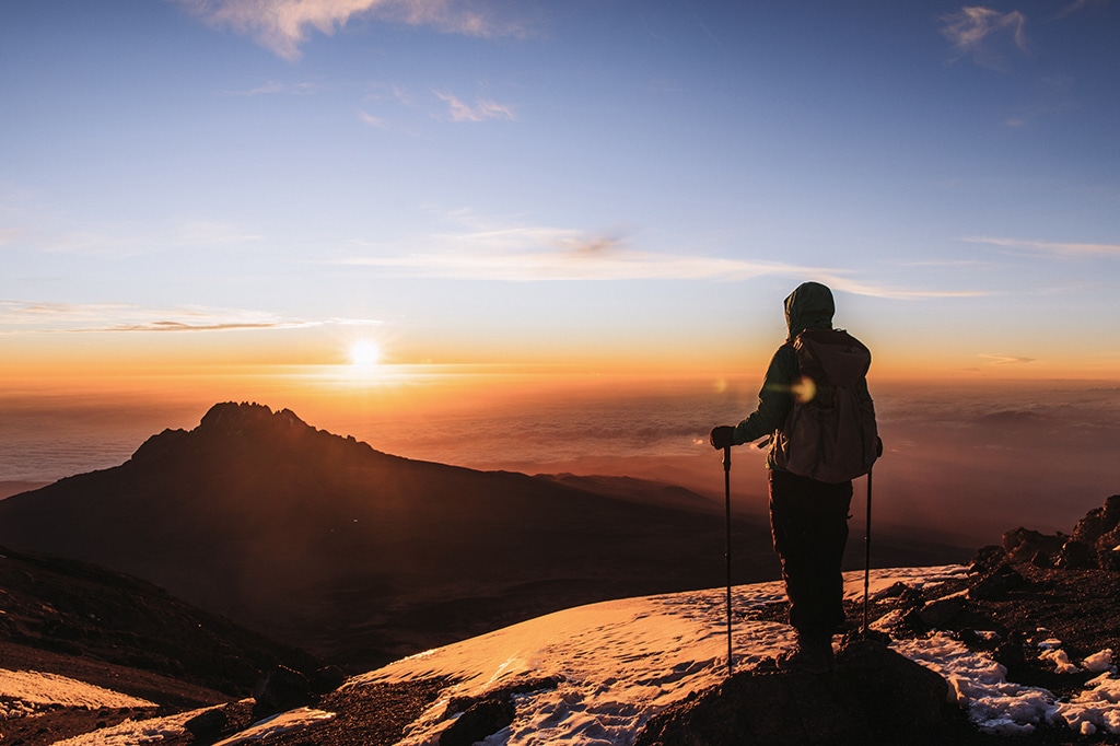 マチャメルートでバックパックとハイキングポールを背負い、美しい黄金色の日の出を眺める女性 マチャメルートでバックパックとハイキングポールを背負い、美しい金色の日の出を眺める女性。