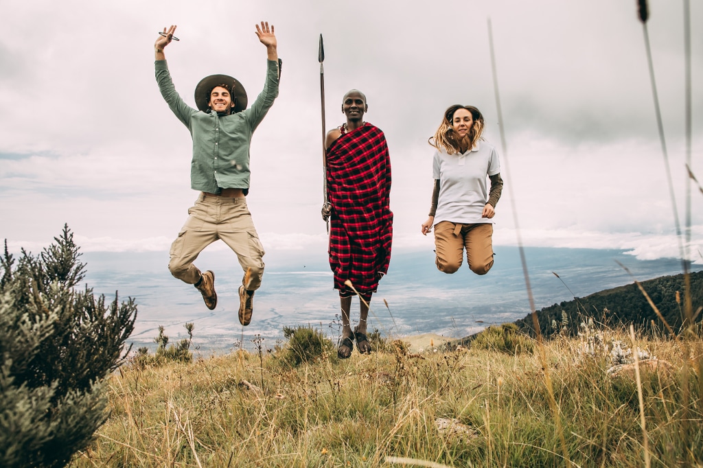 Couple visitors jumping with young Maasai man at Ngorongoro Crater