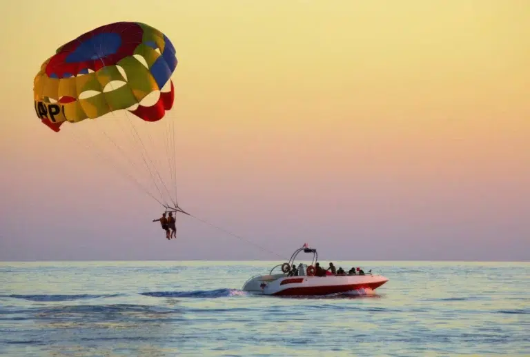 Parasailen bij zonsondergang boven Bwejuu Beach, Zanzibar, met een kleurrijke parachute en een speedboot op het kalme oceaanwater.