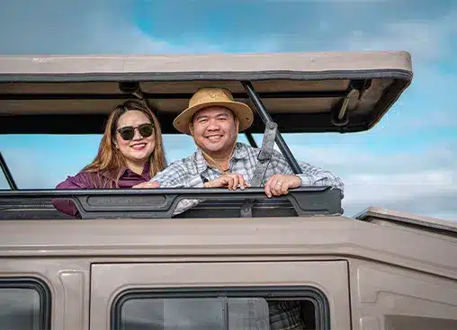 一对笑容满面的夫妇站在敞篷车里,在湛蓝的天空下享受着野生动物园之旅。.