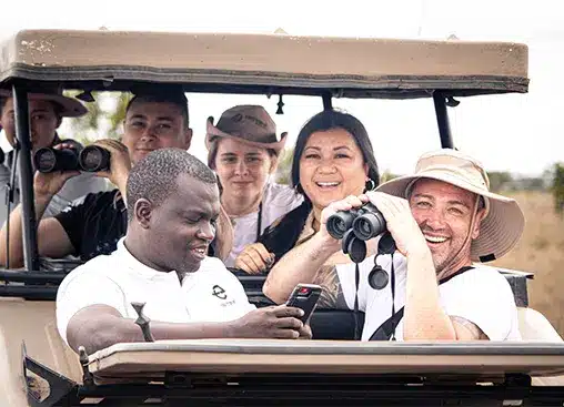 Un groupe de personnes à bord d'une jeep de safari, souriantes et utilisant des jumelles, profitant de l'observation de la faune sauvage dans un cadre naturel.