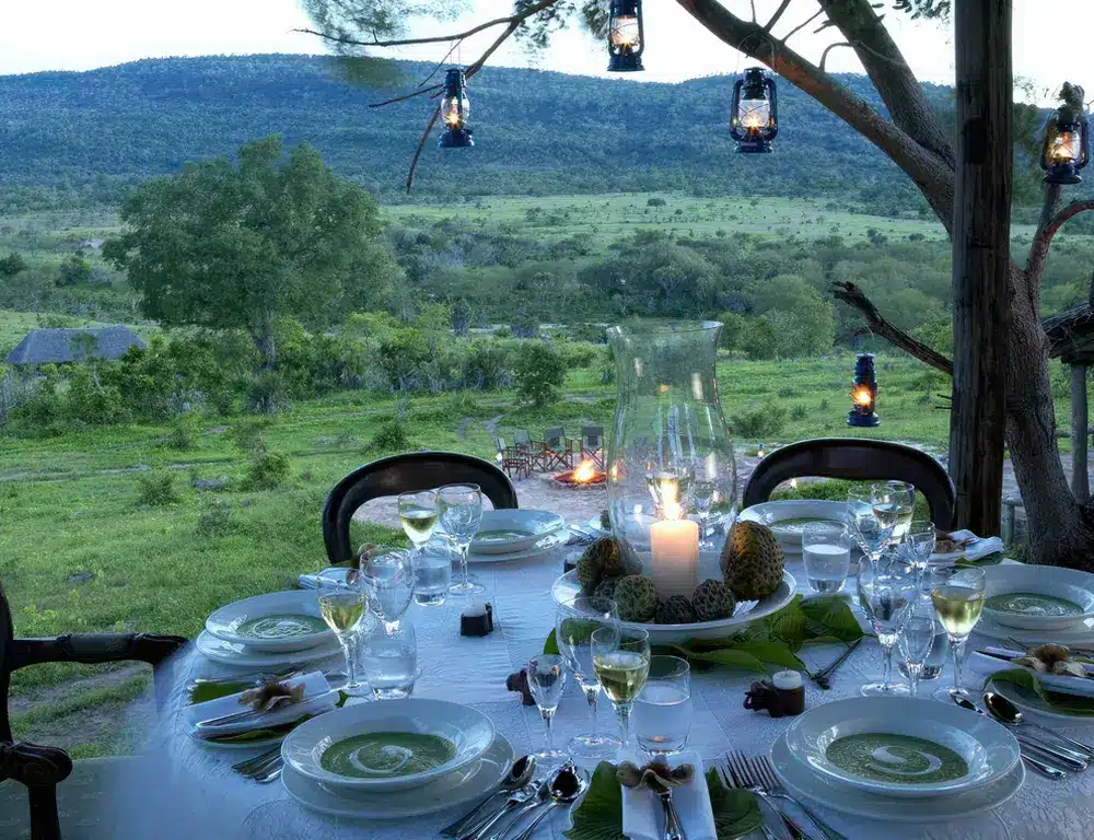 タンザニアのベホベホにある屋外ダイニングのセットアップ。緑豊かな風景と美しい景色を眺めながら優雅にセッティングされたテーブルが特徴です。.