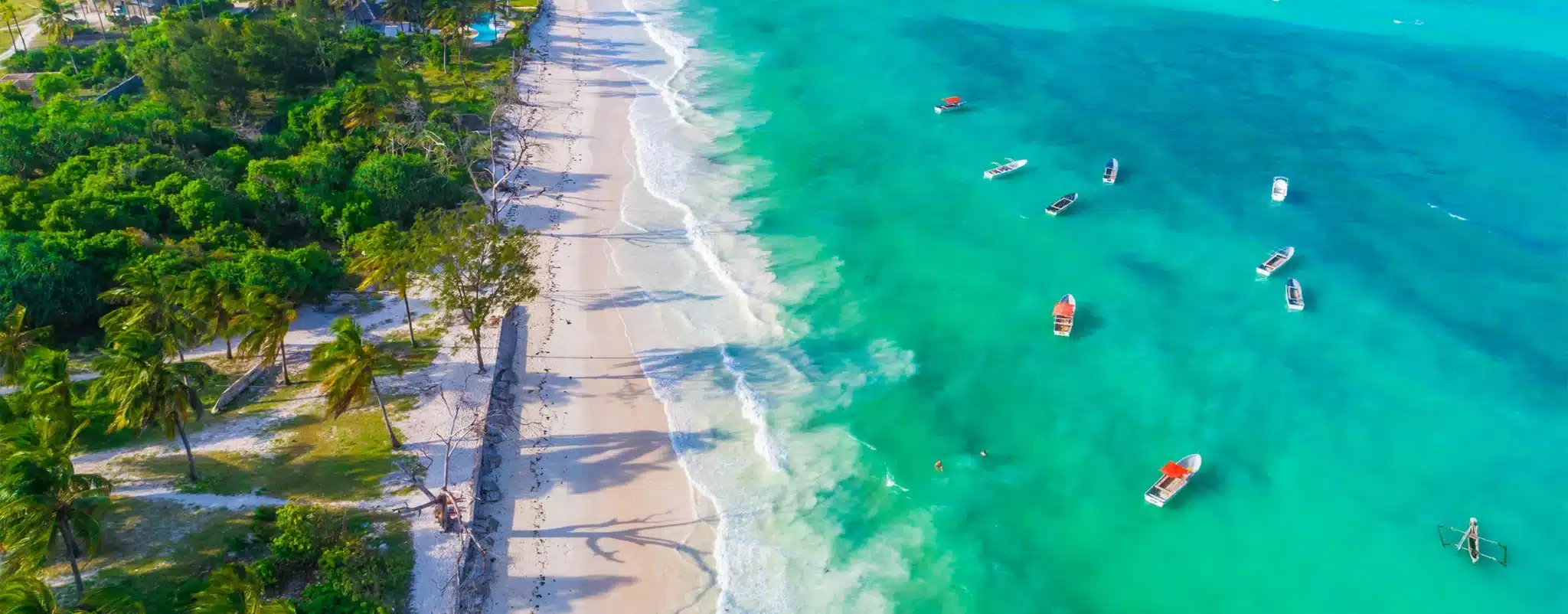 Aerial view of Paje Beach, Zanzibar, showcasing turquoise waters, white sand, and scattered boats along the shoreline.