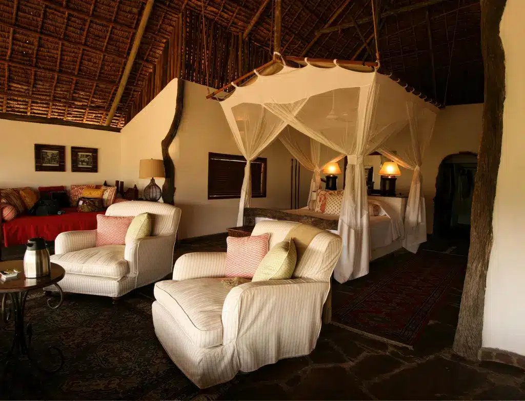 タンザニアのベホベホにある豪華なサファリロッジの部屋。天蓋付きベッド、快適な座席、素朴な装飾が特徴です。.