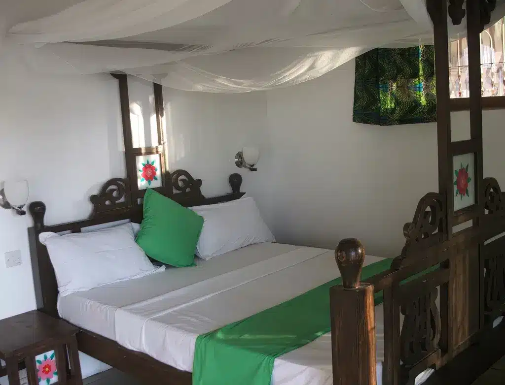 Gemütliches Zimmer in den Bomani Beach Bungalows, Tansania, mit Holzbett, weißer Bettwäsche, grünen Akzenten und dekorativer Ausstattung...