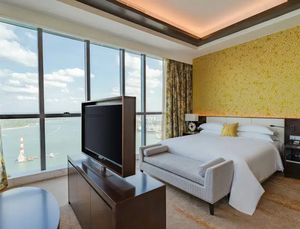 Современный номер в отеле Johari Rotana, Дар-эс-Салам, с видом на океан, большой кроватью, телевизором и элегантным декором.