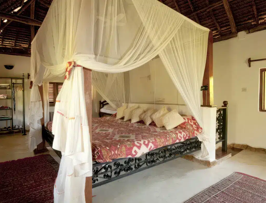 Gezellige kamer in Kinasi Lodge, Tanzania, met een hemelbed met transparante gordijnen, kleurrijk beddengoed en een rustieke inrichting.