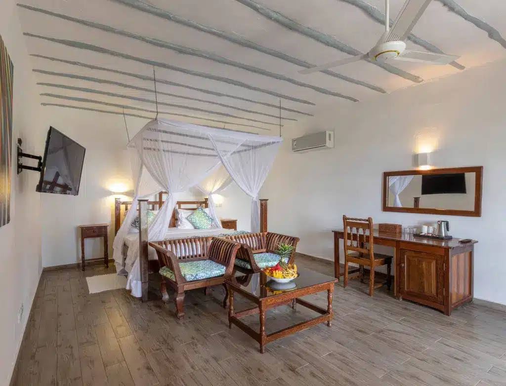 Chambre spacieuse au Kiwengwa Beach Resort, avec lit à baldaquin, meubles en bois, télévision et ventilateur de plafond, idéale pour...