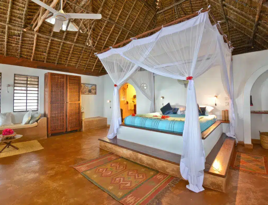 Просторный номер в отеле Matemwe Lodge в Танзании, оборудованный кроватью с балдахином, оформленный в деревенском стиле и с соломенным потолком, создающий атмосферу тропического отдыха.
