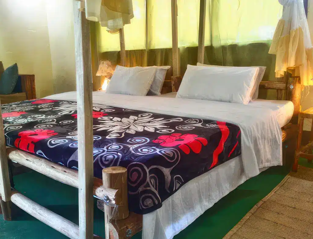 坦桑尼亚米库米野生动物园旅馆的一间舒适客房，配有一张双人床、色彩鲜艳的床上用品和质朴的木质装饰。.