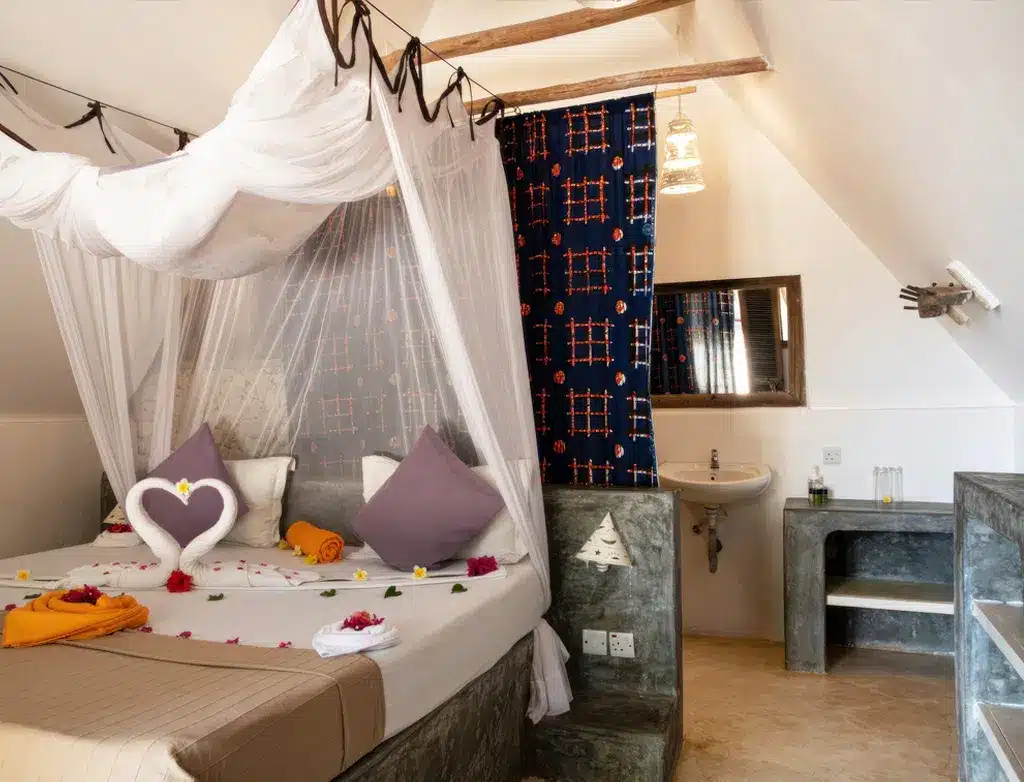 Gezellige hotelkamer met een hemelbed, decoratieve kussens en een handdoekenset met zwanenmotief, en een stijlvolle wastafel.