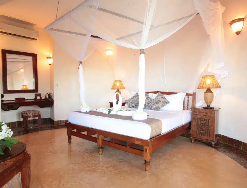 Chambre élégante à l'Ocean Paradise Resort & Spa, à Zanzibar, avec un lit à baldaquin, un éclairage chaleureux et une décoration tropicale.