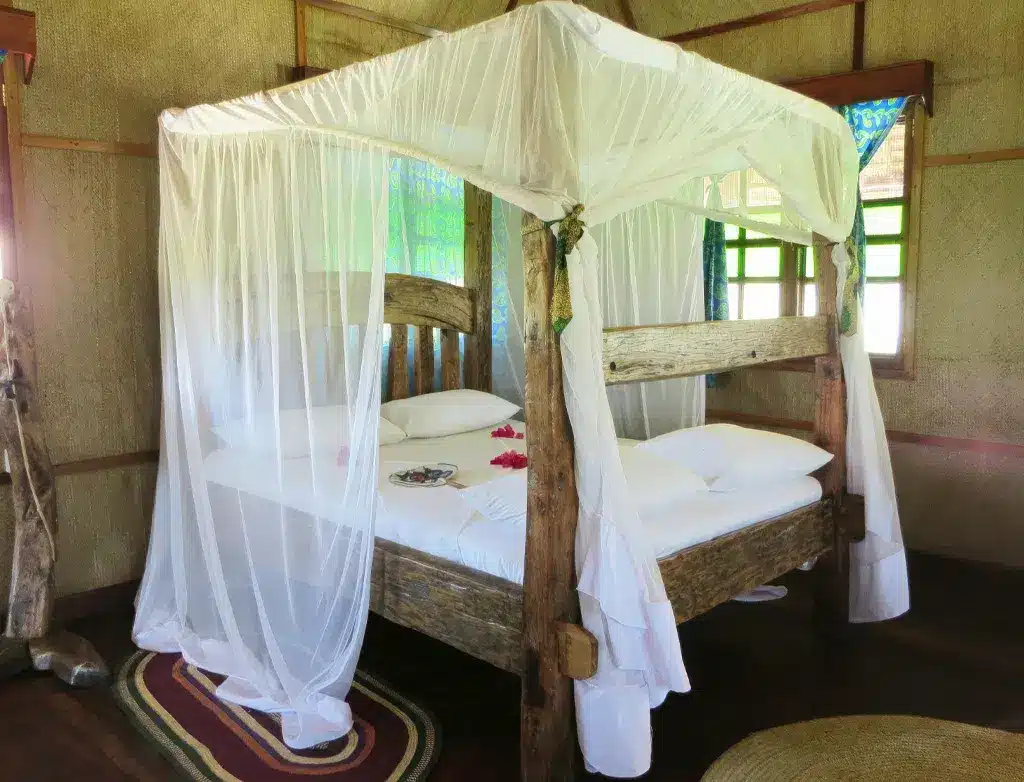 Gezellige lodgekamer in Pemba, Tanzania, met een rustiek houten hemelbed, gedrapeerd met witte klamboe en kleurrijke decoratie.