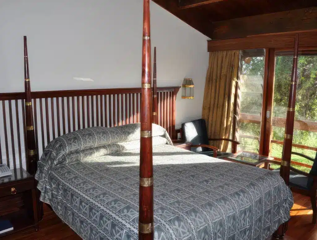 Gezellige lodgekamer met een hemelbed, houten accenten en een groot raam met uitzicht op weelderig groen in Tanzania.
