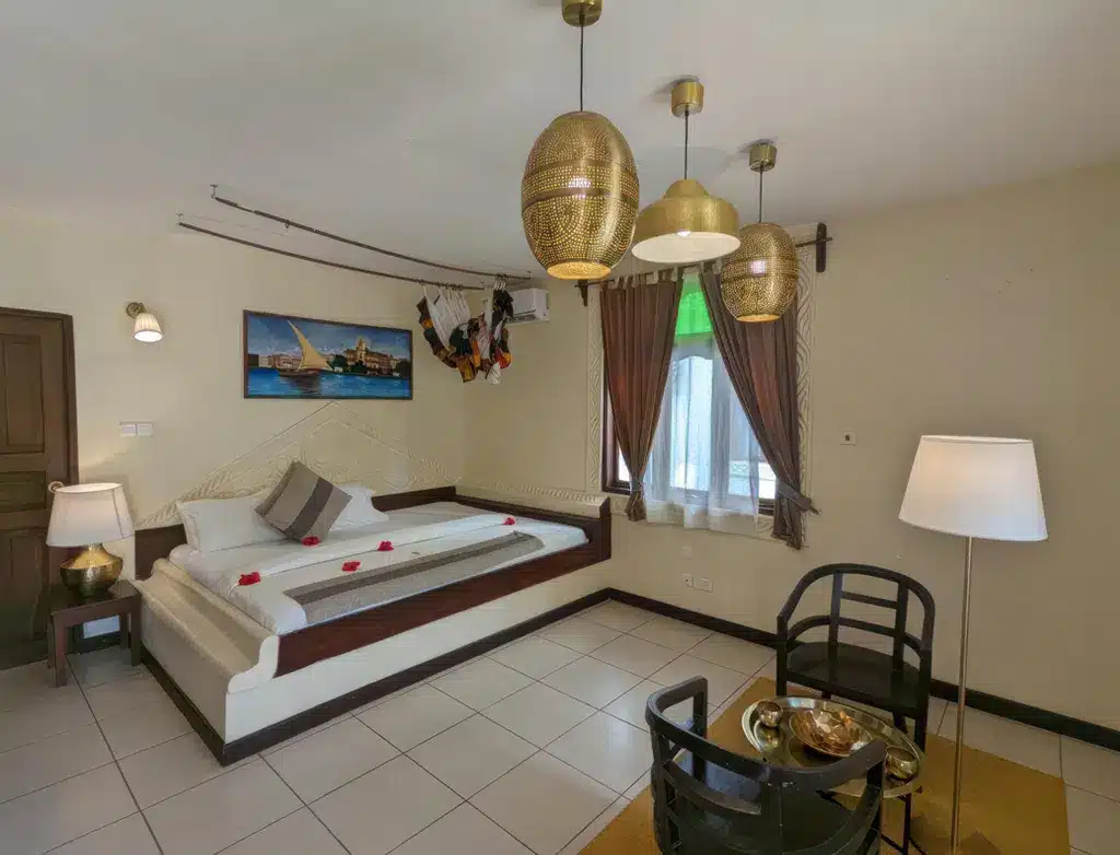 Mysigt hotellrum med dubbelsäng, dekorativ belysning och sittgrupp på Smiles Beach Hotel, Tanzania.