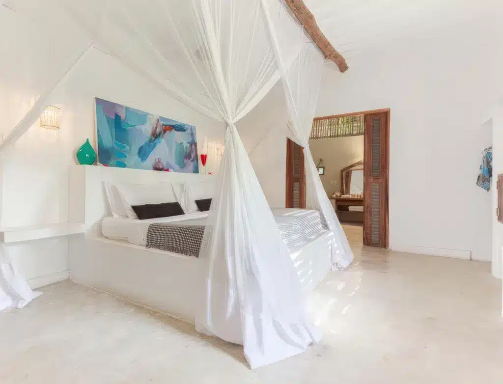 Ljust, luftigt sovrum med himmelssäng, vit inredning och färgglad väggkonst på Upendo Beach, Zanzibar.