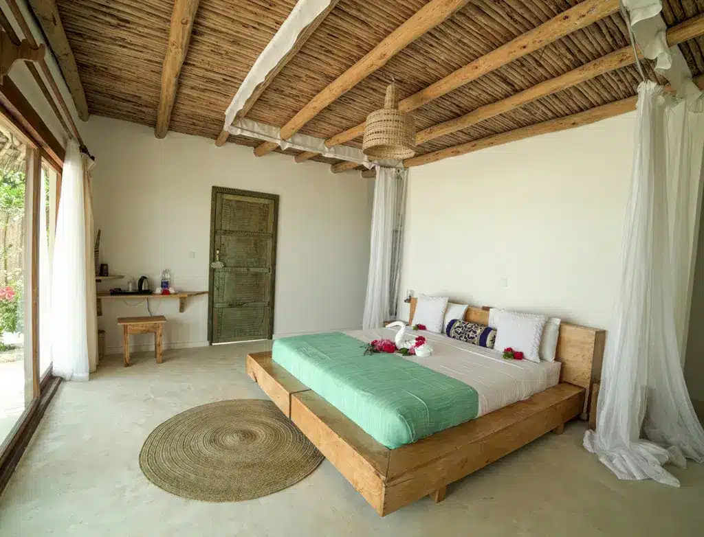 Cozy hotel room with wooden ceiling, large bed, decorative swans, and natural light at Zanbluu Beach Hotel, Tanzania.