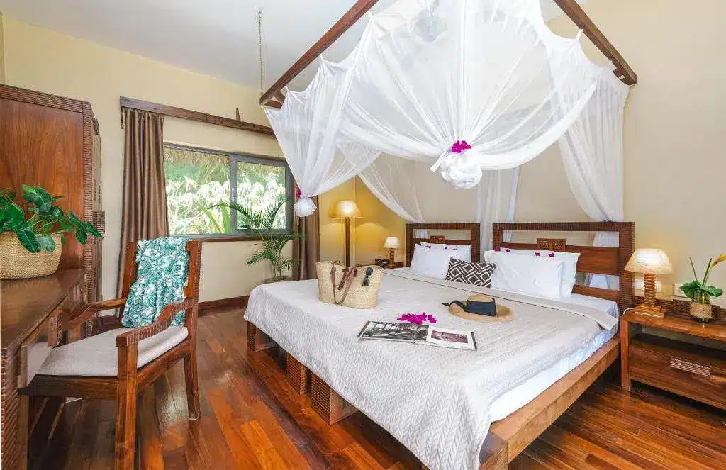 Luxurious resort room with canopy bed, wooden decor, and tropical accents at Zanzi Resort. Cozy and inviting atmosphere.