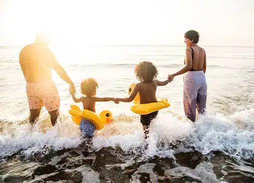 一家人手牵手,在日落时分走向大海,孩子们都戴着充气游泳圈。.