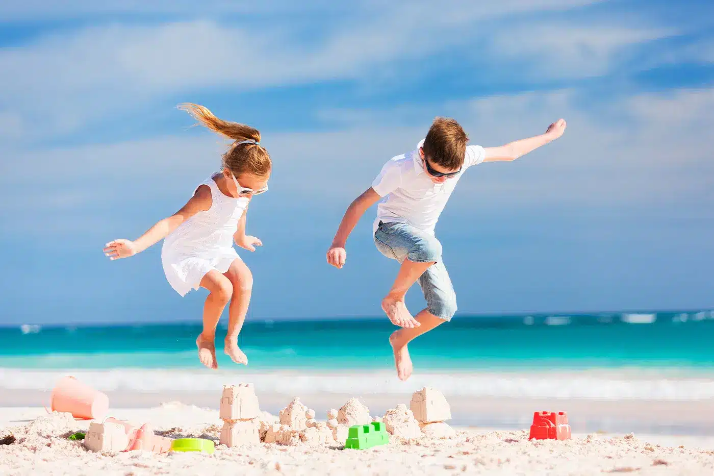 Kinder springen vergnügt auf einem Sandstrand in Sansibar unter strahlend blauem Himmel, während sich türkisfarbene Meereswellen ergießen.