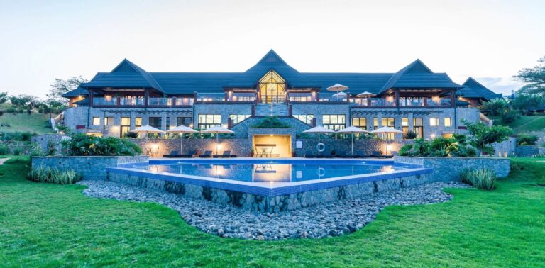 Luxuriöse Villa mit großem Pool, umgeben von üppigem Grün, unter klarem Abendhimmel.