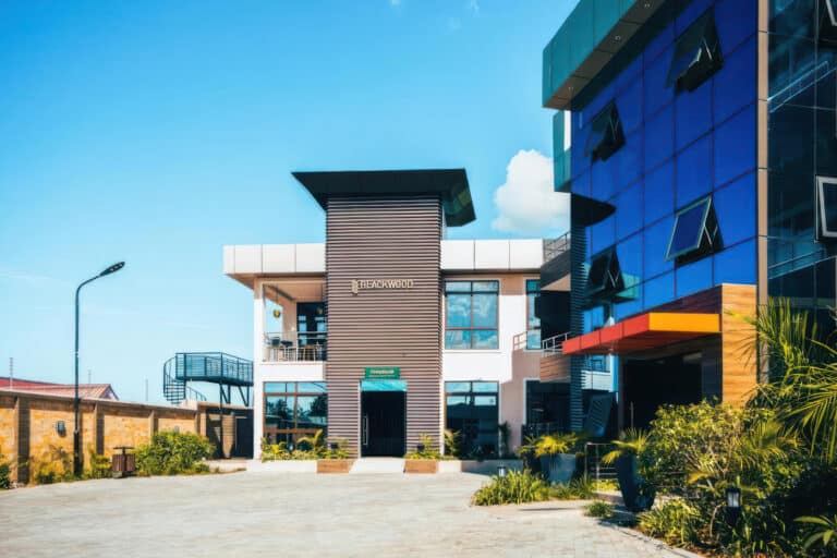 Modern office building with glass facade, blue sky, and landscaped entrance, featuring "TECHNOLOGY" sign above the door.