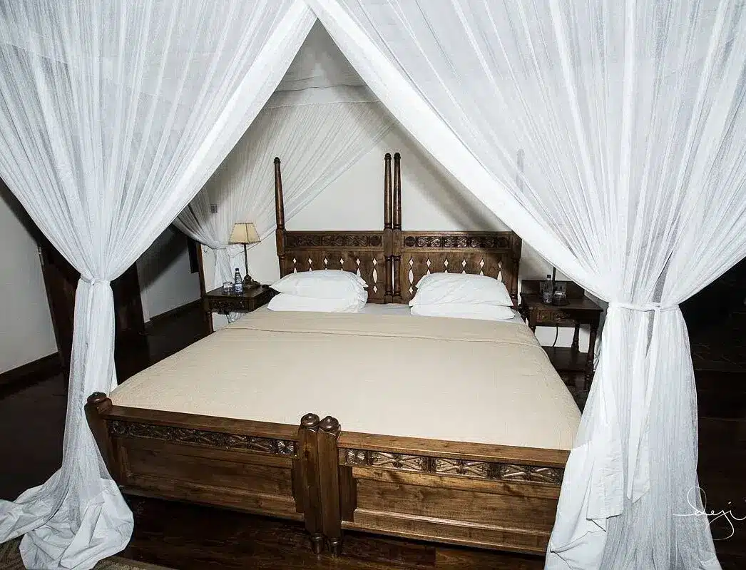 Chambre élégante avec un lit à baldaquin en bois sculpté, des rideaux blancs et un éclairage doux, créant une ambiance chaleureuse et luxueuse.
