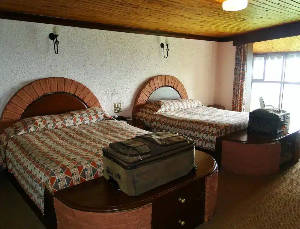 Rum på Ngorongoro Sopa Lodge med två sängar, mönstrade överkast, trätak och stort fönster med naturskön utsikt.