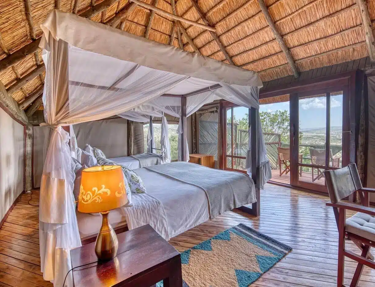 Luxuriöses Lodge-Zimmer mit Himmelbett, Holzdekor und Balkon mit Blick auf die Serengeti-Landschaft in der Soroi Serengeti Lodge.