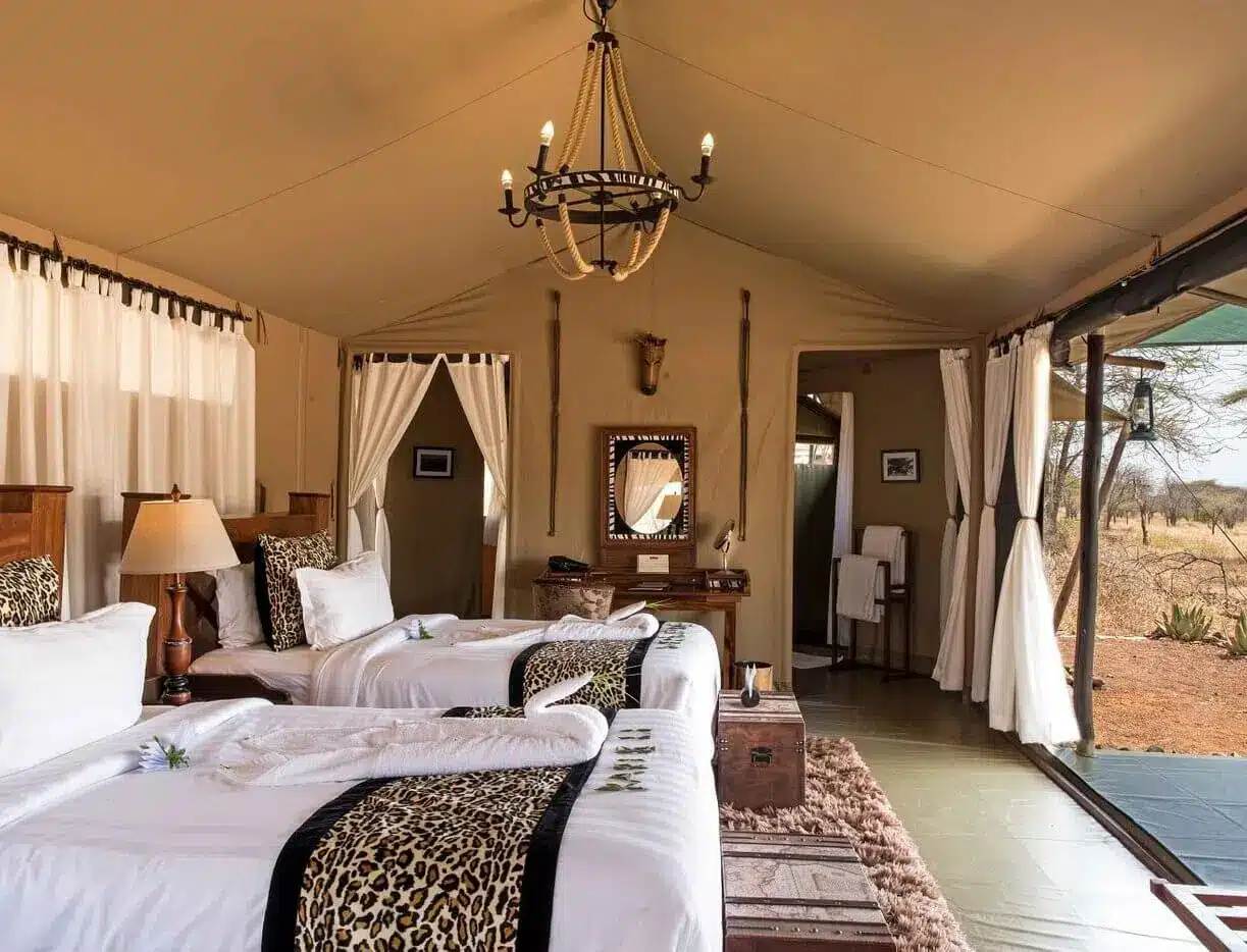 Luxuriöses Safari-Zelt-Interieur mit zwei Einzelbetten, Akzenten im Leopardenmuster, Holzmöbeln und Blick auf die Savanne bei...