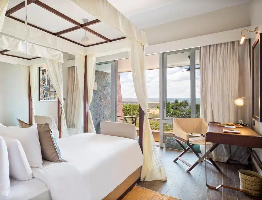 Luxuriöses Serengeti-Hotelzimmer mit Himmelbett, großen Fenstern, Schreibtisch und malerischem Blick auf die Savannenlandschaft.
