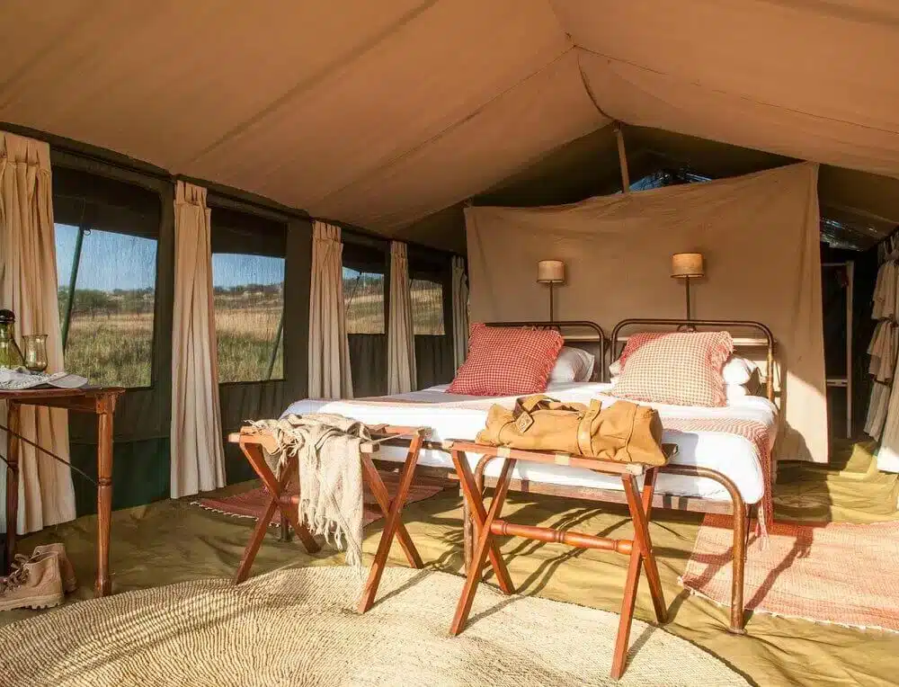 Intérieur luxueux d'une tente safari avec lits jumeaux, mobilier en bois et lumière naturelle au camp du Serengeti.