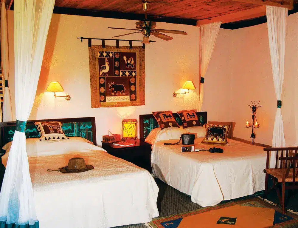 Gezellige kamer in Tarangire Sopa Lodge met twee eenpersoonsbedden, Afrikaanse decoratie, warme verlichting en een rustiek houten plafond.