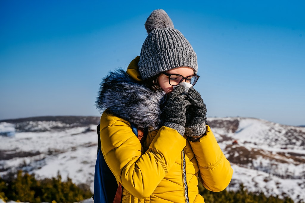 Portrait of young woman blowing nose on snowy cold mountain