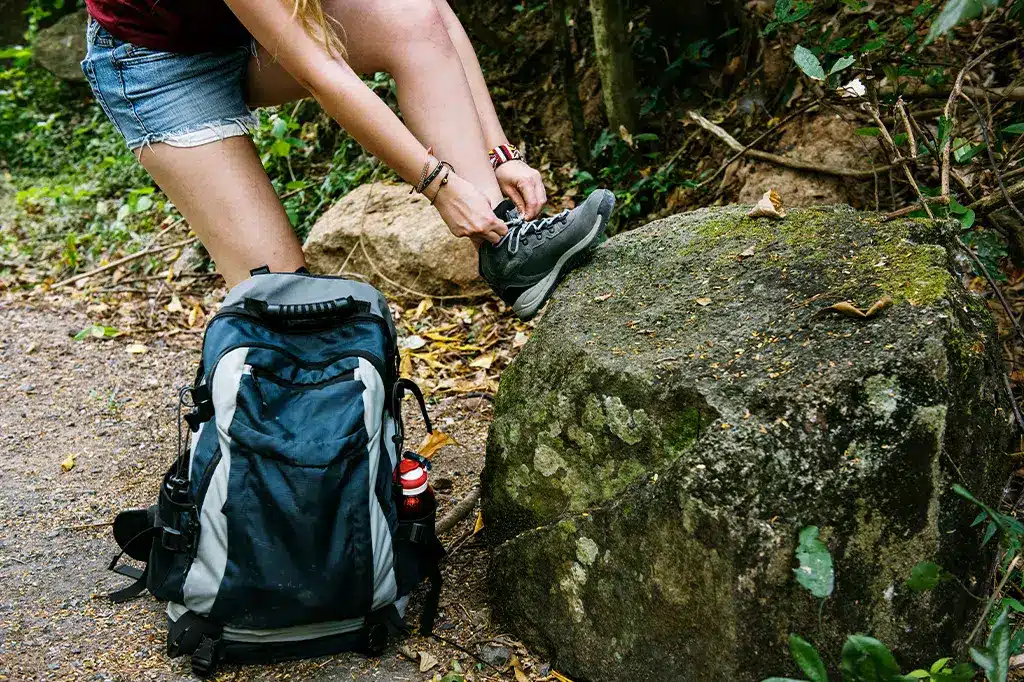 Jonge wandelaar die haar schoenveters strikt terwijl ze haar rugzak laag houdt.jpg