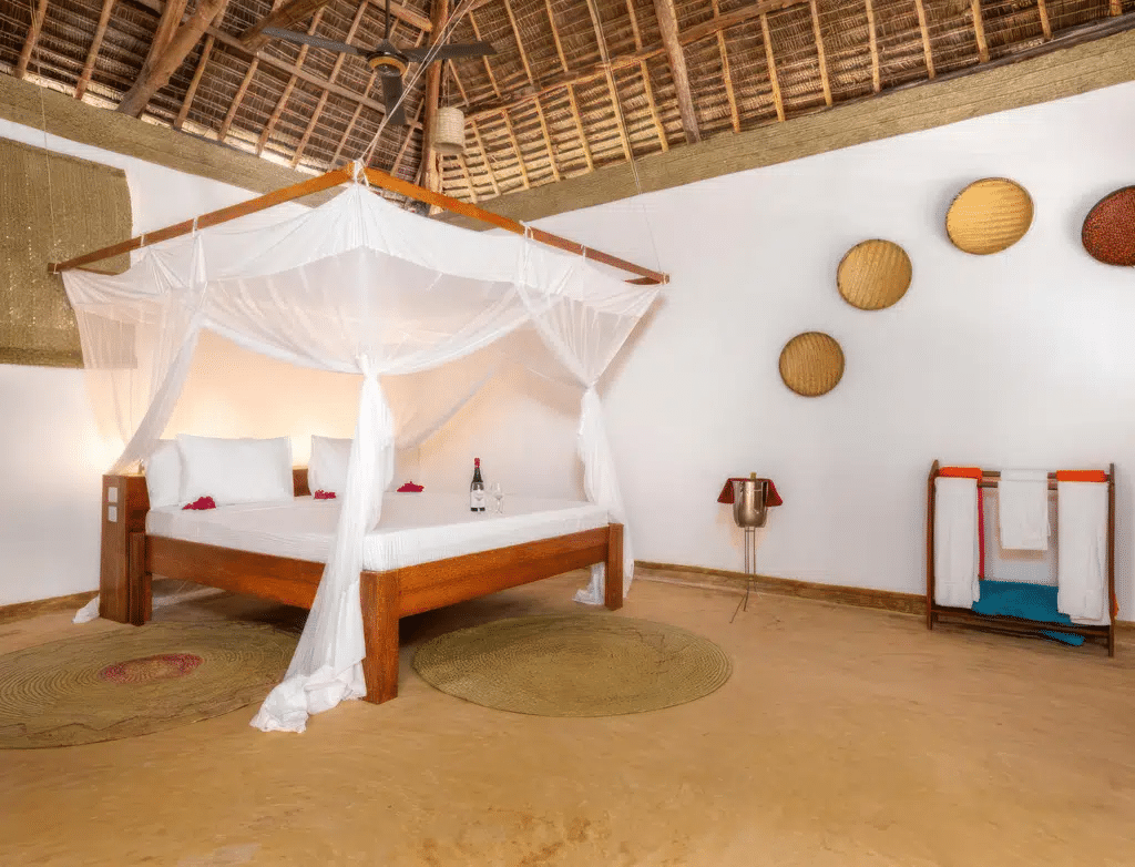 Rustikt sovrum med himmelssäng, vita sängkläder och dekorativa väggkorgar, vilket skapar en mysig, tropisk tillflyktsortsatmosfär.