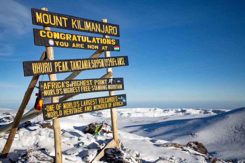 Mount Kilimanjaro summit signs with snow-covered landscape under a clear blue sky.