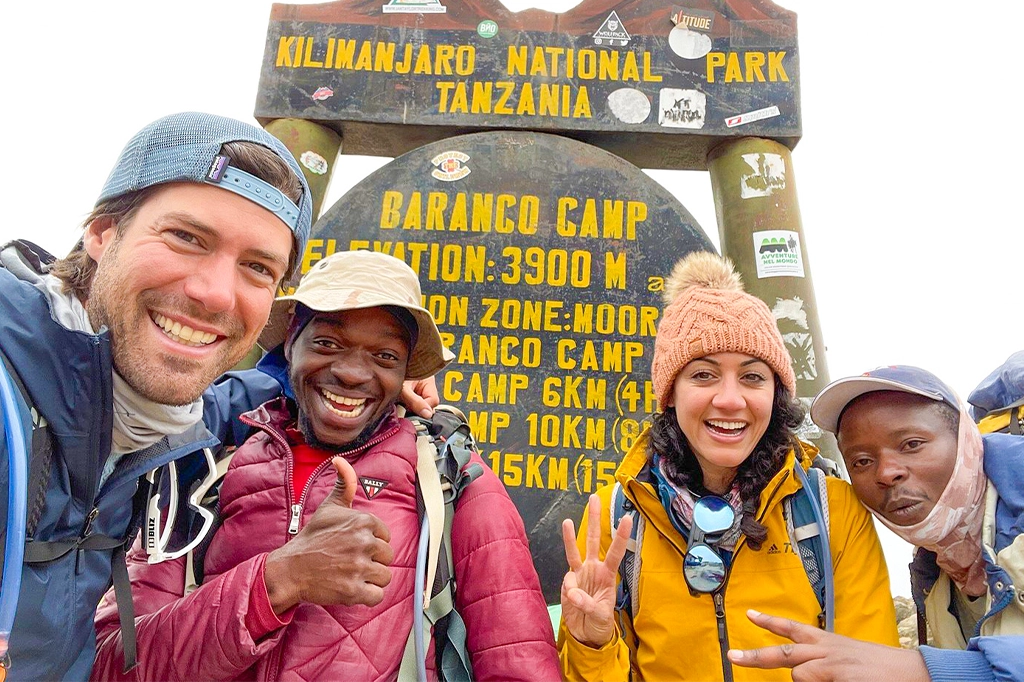 Blije wandelaars en Easy Travel-berggidsen poseren bij het Baranco Camp-bord op de Kilimanjaro Blije wandelaars en Easy Travel-berggidsen poseren bij het Baranco Camp-bord op de Kilimanjaro