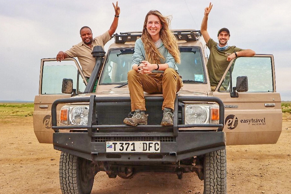 Een gelukkige toerist zit vooraan in een Easy Travel-safarivoertuig en poseert met een Easy Travel-gids en een andere toerist die vredesgebaren maakt. Een gelukkige toerist zit vooraan in een Easy Travel-safarivoertuig, poseert met een Easy Travel-gids en een andere toerist die vredesgebaren maakt.