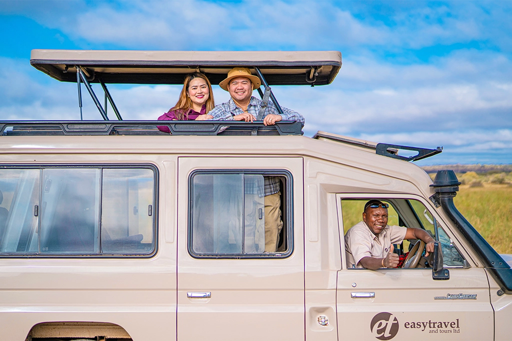 Happy tourists smiling from an Easy Travel safari vehicle roof with their guide giving a thumbs-up