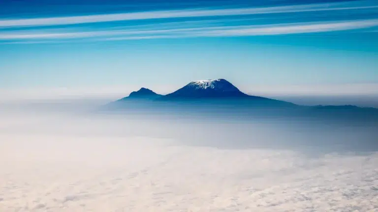 Il Monte Kilimanjaro si erge sopra una coltre di nuvole sotto un cielo blu durante la salita di 7 giorni sul Kilimanjaro Machame Route.