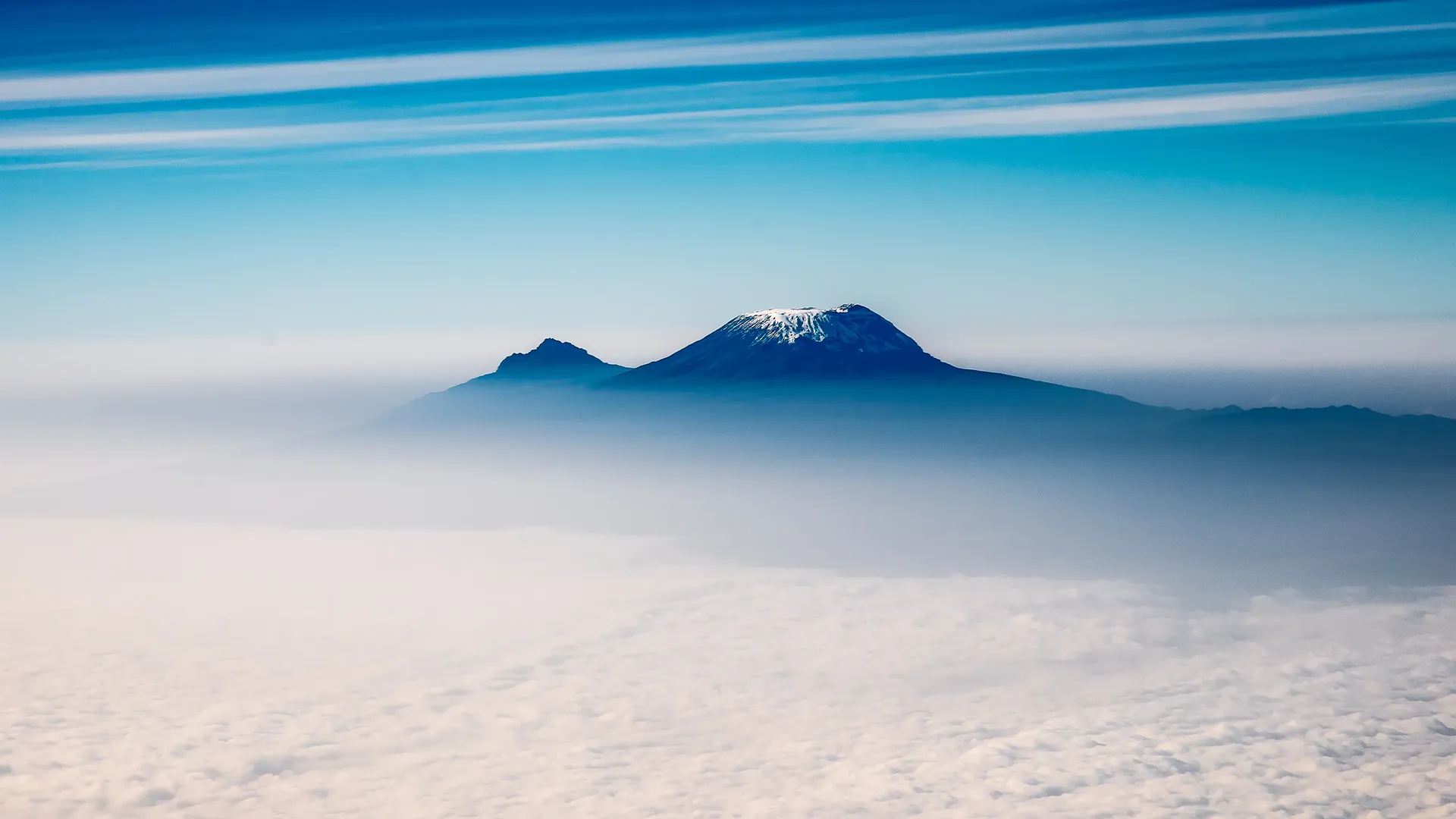 Mount Kilimanjaro rises above a blanket of clouds under a blue sky duing Kilimanjaro Machame Route 7 Days climb.
