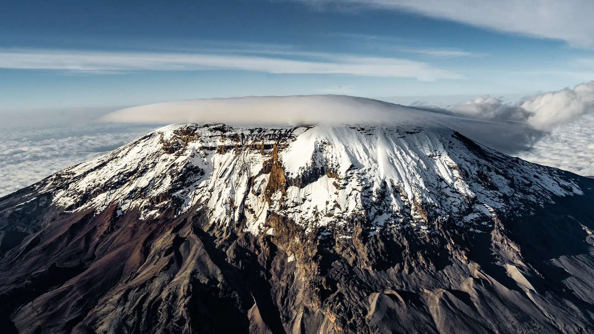 Snow-capped Mount Kilimanjaro rises above the clouds with a soft cloud cap over the summit during Marangu Route Kilimanjaro.