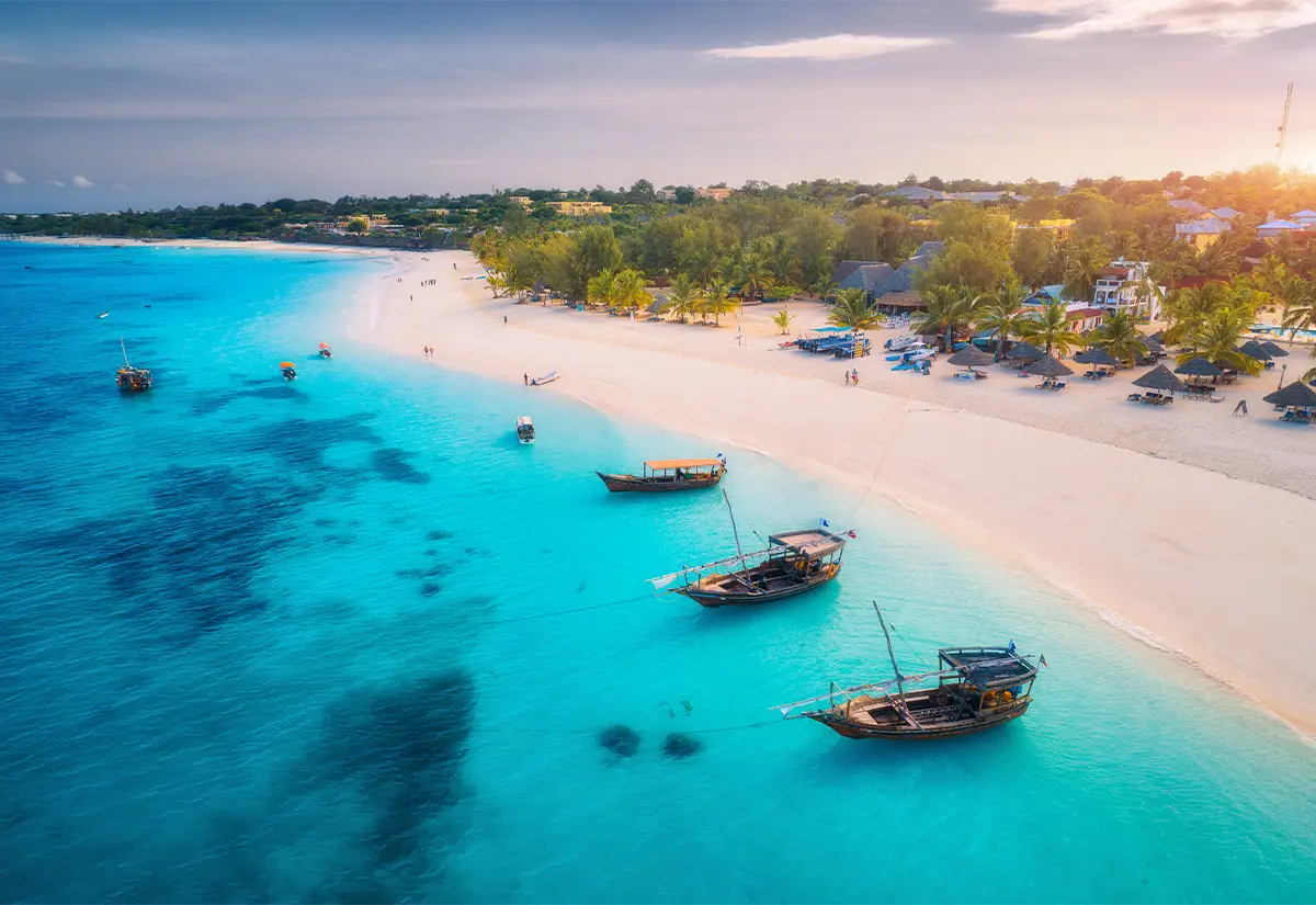 三月至五月 日落时分,晴朗的天空下,宁静的海滩上,碧绿的海水、传统的船只和郁郁葱葱的植被构成了一幅美丽的画卷。.