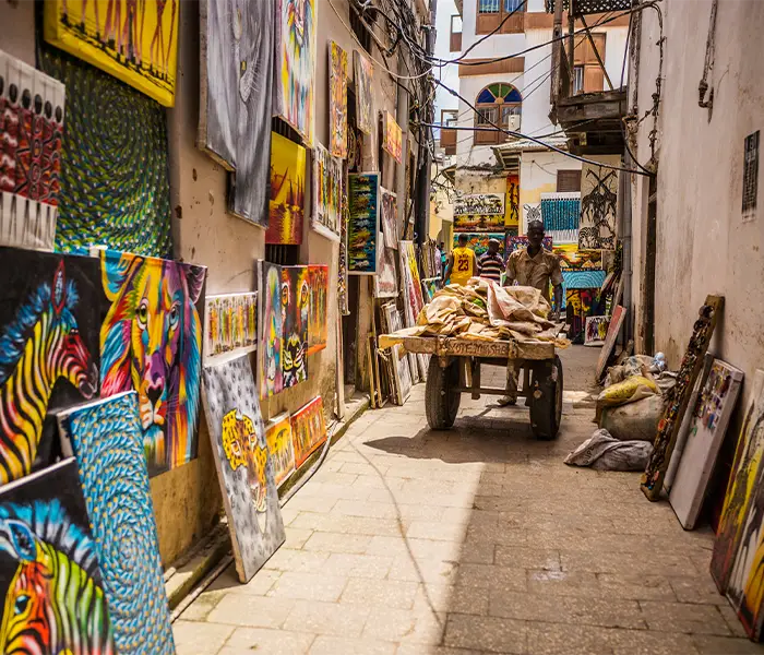 石头城一条狭窄的小巷，墙上挂满了色彩鲜艳的画作，一位男子推着小车，展示着当地的艺术和文化。.