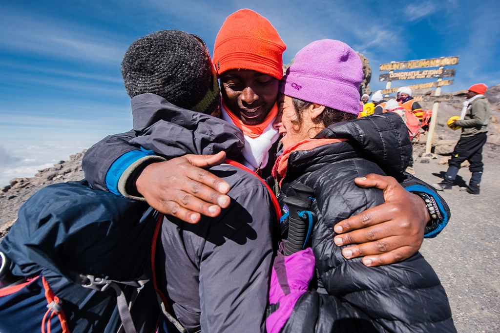 Twee wandelaars omhelzen hun Easy Travel Mountain Guide op de top van de Kilimanjaro Twee wandelaars omhelzen hun Easy Travel Mountain Guide op de top van de Kilimanjaro